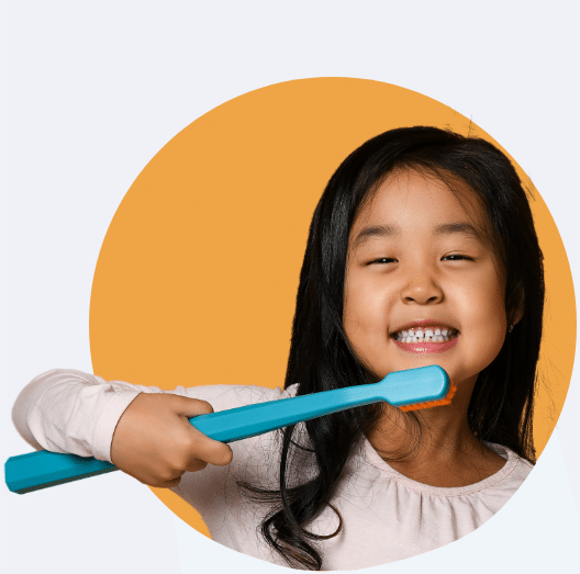 A little girl with dark hair with a giant toothbrush and a big smile to show that this Modesto orthodontist provides early orthodontic treatment