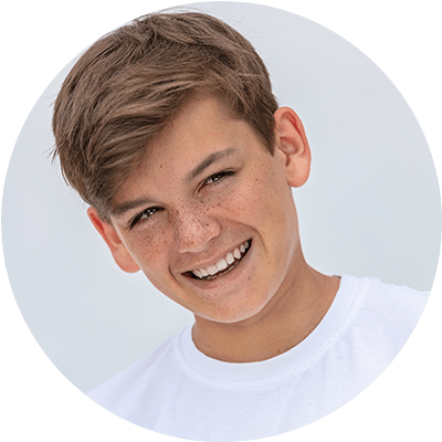A pre teen boy with freckles wearing a white t-shirt and smiling with a perfectly straight smile thanks to his Modesto orthodontist.